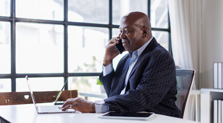 African american Senior Man businessman using mobile phone while working with laptop at workplace office. 
