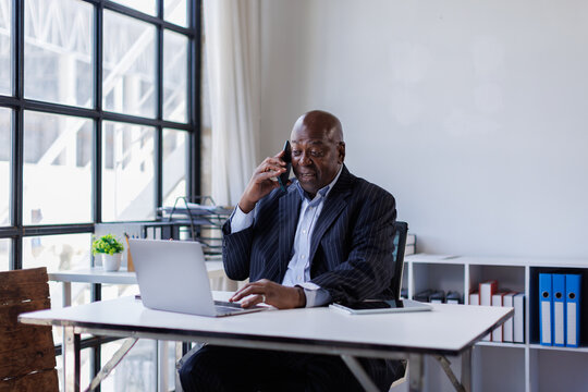 African american Senior Man businessman using mobile phone while working with laptop at workplace office. 
