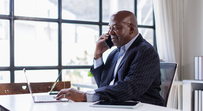 African american Senior Man businessman using mobile phone while working with laptop at workplace office.