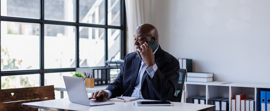African american Senior Man businessman using mobile phone while working with laptop at workplace office. 
