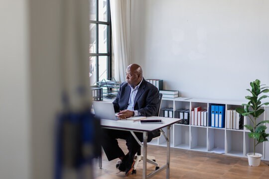 African american Senior Man businessman using mobile phone while working with laptop at workplace office. 
 - Powered by Adobe