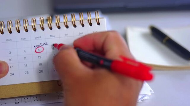 A person marks a calendar with a red marker, circling dates and marking deadlines and progress. Time management, planning, scheduling Important days, Deadlines

