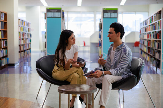 Two university students reading in a cozy library setting, showcasing learning, focus, and collaboration for education and study-themed visuals.
