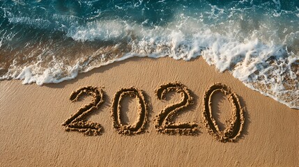 The year 2020 is written in the sand on a beach as the ocean water washes gently over it creating a calming and peaceful scene.