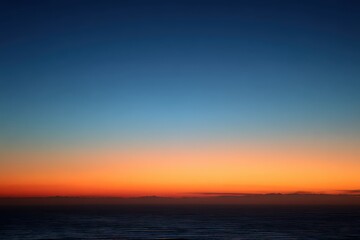 Obraz premium Vibrant Sunrise Horizon with Blue to Orange Gradient Sky Above Silhouetted Landscape and Scattered Clouds Atmospheric Tranquility in Morning Light