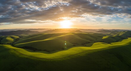Aerial view of rolling green hills, bathed in the warm light of a setting sun under a cloudy sky