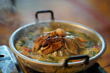 Delicious Asian-style hot pot with bubbling broth, fresh vegetables, and tender meat served in a traditional metal pot on a wooden table