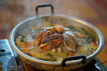 Delicious simmering hot pot with fresh ingredients and steaming broth served in traditional metal pot on a wooden table with vibrant background