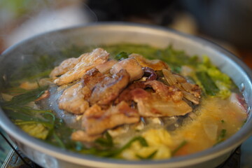 Sizzling Plate of Grilled Meat on a Steaming Hot Pot Surrounded by Fresh Vegetables and Aromatic Herbs in a Cozy Dining Setting