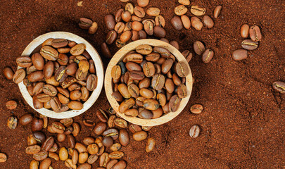 Coffee beans in a wooden bowl placed on a bed of ground coffee. Whole coffee beans are scattered around it