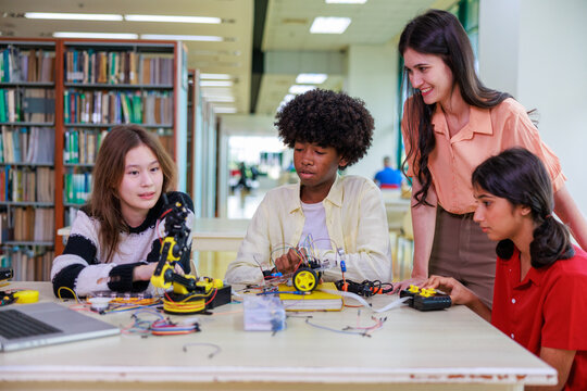 A group of diverse students works with a robotic arm alongside their teacher, showcasing hands-on STEM learning, teamwork, and modern classroom technology. - Powered by Adobe