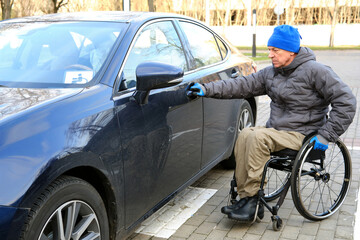 Naklejka premium A man in a wheelchair holds the door handle of his car with his right hand.