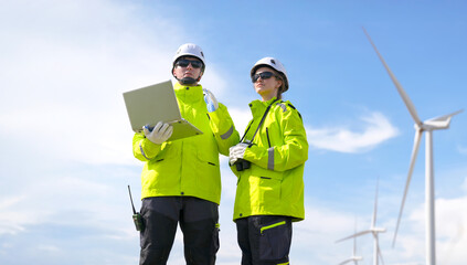 Workers in bright jackets analyze data at a wind farm under a clear blue sky