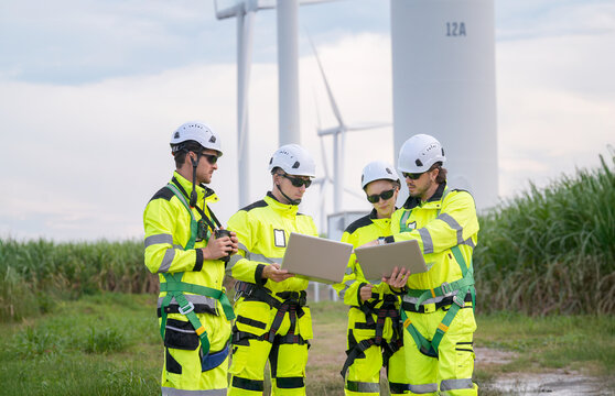 Workers in bright safety gear reviewing data near wind turbines during the day