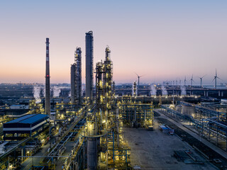 Oil refinery industrial zone with wind turbines under the colorful sky at sunrise.