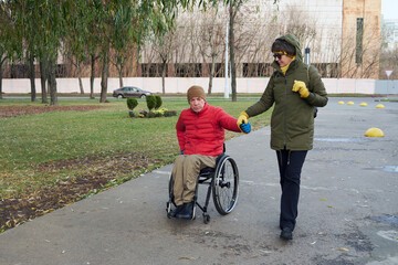 A woman in a green jacket and a man in a wheelchair walk hand in hand