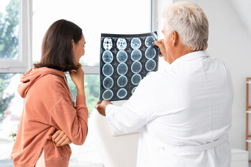 Fototapeta premium Senior doctor showing x-ray scan to young female patient in rehabilitation center