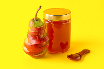 Glass jar of tasty pear jam with wooden spoon on yellow background