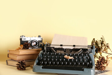 Vintage typewriter, books, pine cones, photo camera and autumn leaves on yellow background