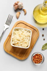 Board with bowl of tasty sauerkraut and ingredients on white background