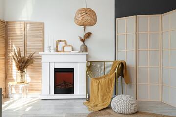 Fototapeta premium Interior of light living room with armchair, fireplace and folding screen