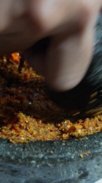 Homemade peanut chili sauce being ground in stone mortar. Traditional Indonesian sambal making process closeup. 4k vertical video