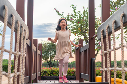 Excited Asian girl laughing happily on the high platform of a wooden playground structure