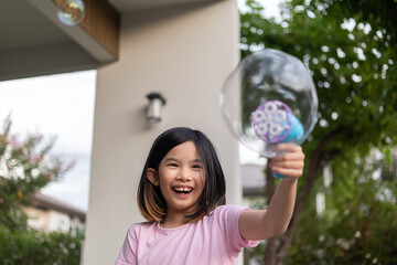 Happy Asian girl smiling and having fun blowing soap bubbles with toy dispenser