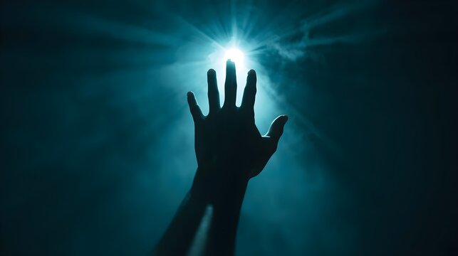 A silhouette of a human hand reaching upwards toward a blinding, intense white light radiating brilliant, volumetric beams through thick blue atmospheric mist or fog.