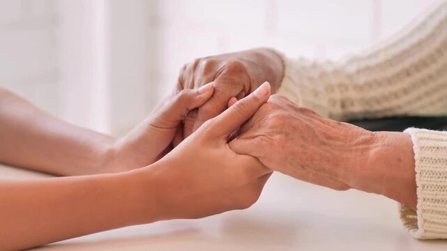 Holding Hands together for Helping and Giving Support. A senior mother sit on sofa while her daughter cover and hold her hands for care and support.