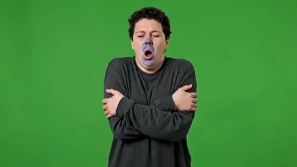 Cold and distraught, a shivering person hugs themselves tightly on a green screen, overwhelmed with sadness and despair in a dramatic, emotive display