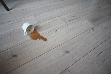 Cup spills coffee on wooden floor at home