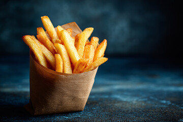 Golden French fries in brown paper bag on blue background fast food takeout