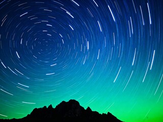 aurora borealis over mountain silhouette with star trails in night sky