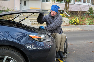 A man in a wheelchair lifts the hood of a car.