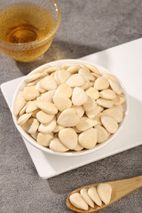 Peeled sliced sweet almonds dried and displayed in bowl with tea on gray background