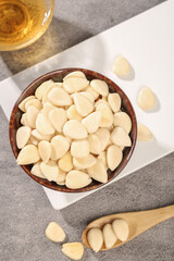 Peeled blanched almonds in bowl with wooden spoon on marble surface - healthy nuts ingredient for cooking and baking