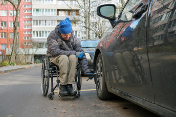 Fototapeta premium A man in a wheelchair checks the tightness of the front wheel of his car with a special wrench.