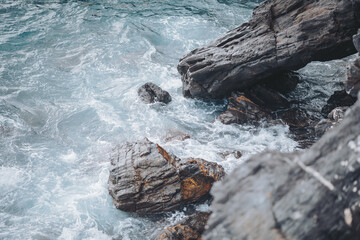 Waves crashing against rocky shoreline at a coastal area during overcast day with gentle ripples and foam creating a serene and natural atmosphere