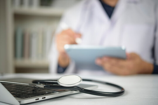 Close up medical equipment tool on notebook desk. Male practitioner holding touchpad stylus blurring back. Electronic health record smart clinic system. Wireless communication insurance idea. - Powered by Adobe