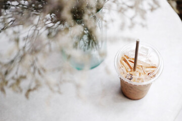 Top view of a plastic glass of ice latte coffee and dry grass flower in vase decorated on white table