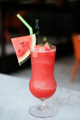 A glass of watermelon smoothie with red star spoon on wooden table in tropical of cafe