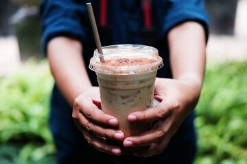 Hand holding a plastic glass of ice latte coffee with chocolate powder on topping 