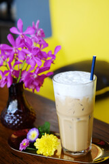 A glass of ice latte coffee with milk foam and pink orchid flower decorated on wooden table