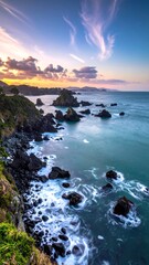 Dramatic coastal view at sunset; rocks, cliffs, and waves under colorful sky.