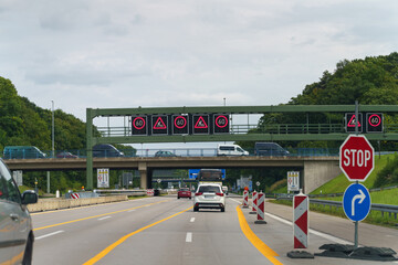 Cars travel on an autobahn, with a speed restriction indicated by overhead electronic signs