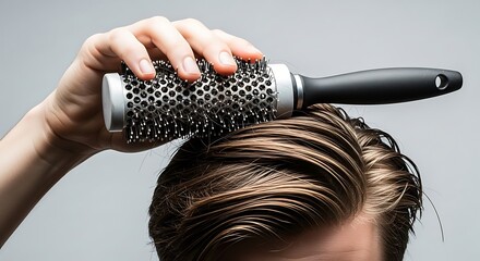 Closeup of a person using a round ceramic hairbrush to style damp, dark brown hair against a light grayBackground image