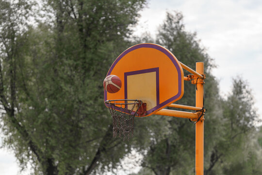 Orange backboard and basketball in mid-air over the net capture an outdoor game moment in the park on a hazy afternoon