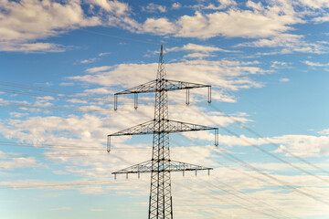 Power transmission tower stands tall against a backdrop of blue sky and fluffy white clouds on a bright sunny day
