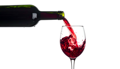A bottle of red liquid pours into a clear wine glass, creating splashes against a black backdrop